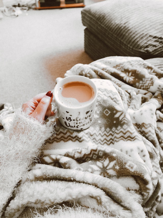 woman sitting under a blanket holding a cup of tea
